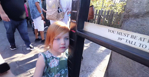 A Little Girl Is Standing Next To A Sign That Says You Must Be At 39 Inches Tall GIF