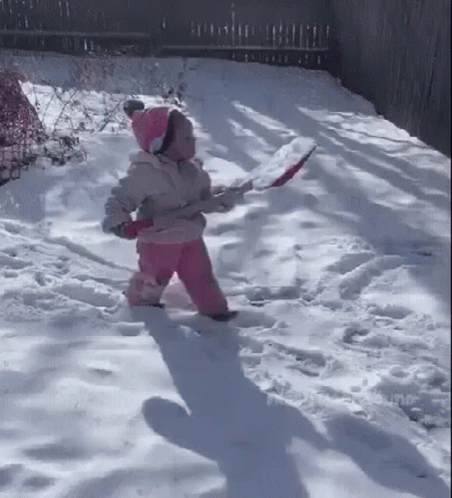 A Little Girl Is Walking Through The Snow While Holding A Shovel . GIF