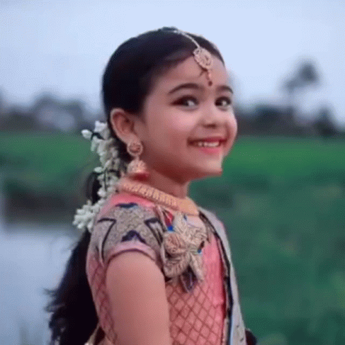 A Little Girl Is Wearing A Pink Dress And Smiling . GIF