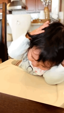 A Little Girl Laying On A Table With Her Head Resting On A Pillow GIF