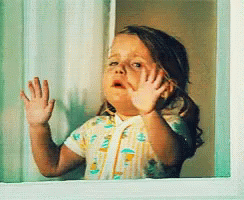 A Little Girl Looking Out Of A Window With Her Hands On The Glass GIF