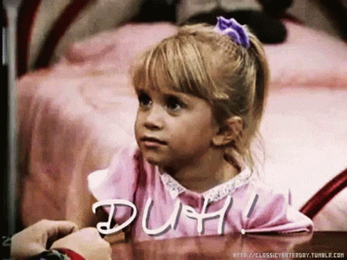 A Little Girl Sitting At A Table With The Word Duh Written On The Table GIF