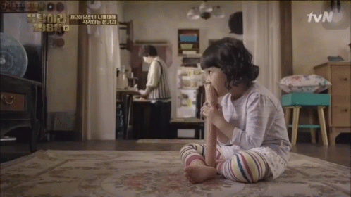 A Little Girl Sitting On A Rug With A Tvn Logo On The Wall Behind Her GIF
