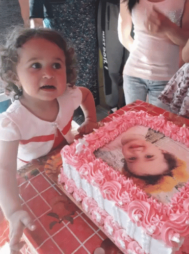 A Little Girl Stands In Front Of A Cake With A Picture Of A Girl On It GIF