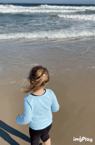 A Little Girl Stands On A Beach Looking At The Ocean With Imgplay At The Bottom GIF