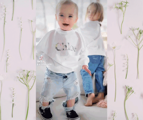 A Little Girl Wearing A Bell Sleeve Top And Ripped Jeans Is Standing In A Pile Of Leaves And Flowers GIF