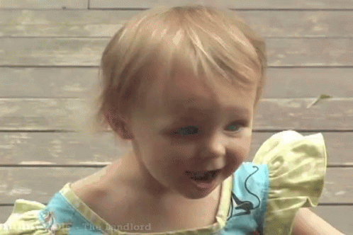 A Little Girl Wearing A Blue And Yellow Dress Is Smiling . GIF