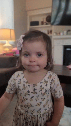 A Little Girl Wearing A Floral Dress With A Bow In Her Hair GIF