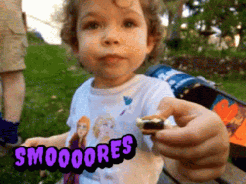 A Little Girl Wearing A Frozen Shirt Is Holding A Smores In Her Hand GIF