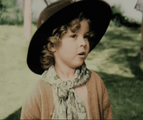 A Little Girl Wearing A Hat And Scarf Looks To The Side GIF