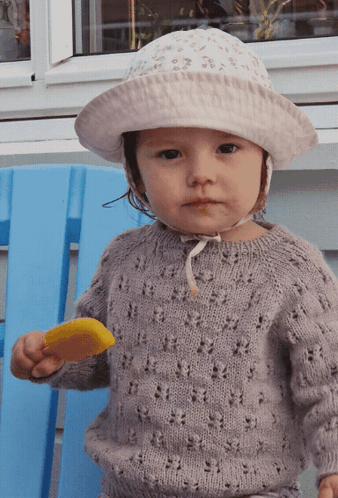 A Little Girl Wearing A Hat And Sweater Is Holding An Ice Cream Bar GIF