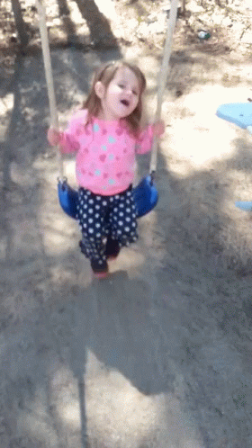 A Little Girl Wearing A Pink Shirt And Blue Polka Dot Pants Is Swinging On A Blue Swing GIF