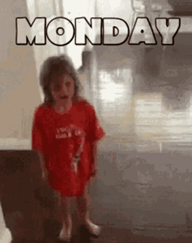 A Little Girl Wearing A Red Shirt Is Standing In Front Of A Monday Sign . GIF