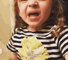 A Little Girl Wearing A Striped Shirt With A Yellow Flower On It Is Making A Funny Face . GIF