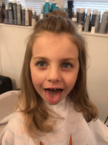 A Little Girl Wearing A White Cape With A Unicorn On It Sticks Out Her Tongue GIF