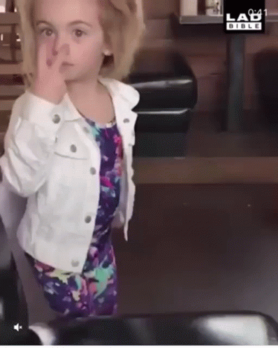 A Little Girl Wearing A White Jacket And A Purple Dress Is Giving The Middle Finger GIF