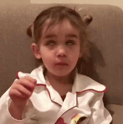 A Little Girl Wearing A White Jacket With A Red Collar Is Sitting On A Couch GIF