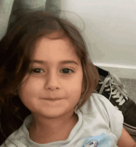 A Little Girl Wearing A White Shirt With A Picture Of A Horse On It Looks At The Camera GIF