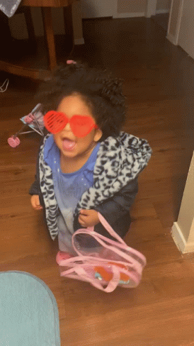 A Little Girl Wearing Heart Shaped Sunglasses And Holding A Pink Bag GIF
