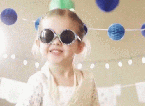 A Little Girl Wearing Sunglasses And A Party Hat Is Dancing At A Birthday Party . GIF