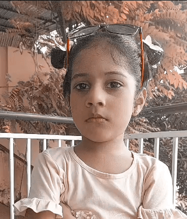 A Little Girl Wearing Sunglasses And Pigtails Is Looking At The Camera GIF