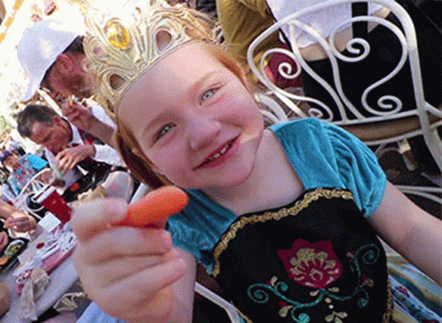 A Little Girl With A Crown On Her Head Is Holding A Carrot GIF