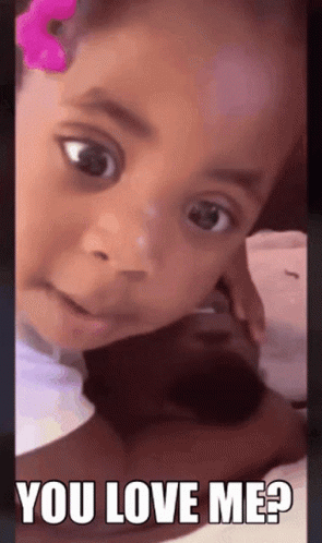 A Little Girl With A Pink Flower In Her Hair Is Looking At The Camera And Says You Love Me GIF