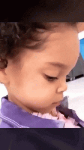 A Little Girl With Curly Hair Is Wearing A Purple Jacket And Looking At The Camera . GIF
