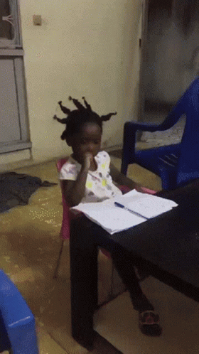 A Little Girl With Dreadlocks Sits At A Table With A Pen In Her Hand GIF