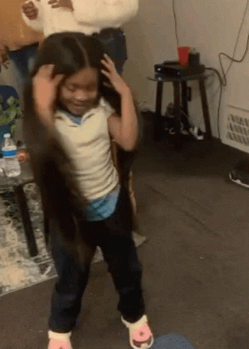 A Little Girl With Long Hair Is Dancing In A Living Room With A Woman Holding Her Hair . GIF