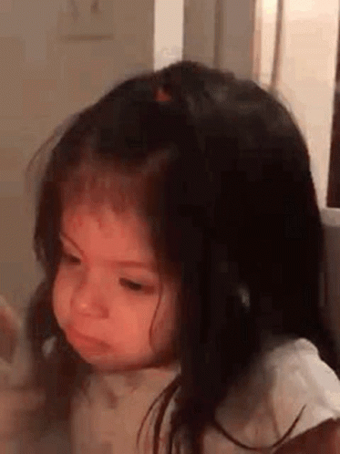 A Little Girl With Long Hair Is Making A Funny Face While Sitting In A Chair . GIF