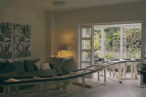 A Living Room With A Couch And A Table With A Wooden Railing Going Through It GIF