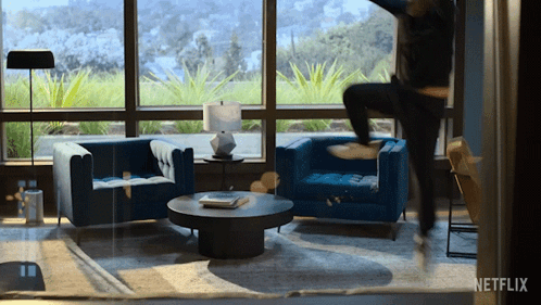 A Living Room With Blue Chairs And A Coffee Table With A Netflix Logo In The Corner GIF