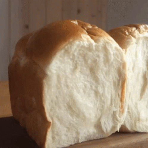 A Loaf Of Bread That Has Been Cut In Half Sits On A Wooden Table GIF