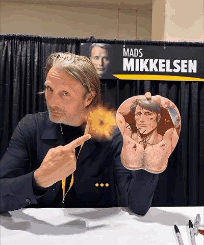 A Mads Mikkelsen Sign Hangs Above A Man 'S Arm GIF