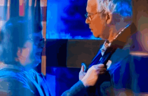 A Man Adjusts His Tie While A Woman Looks On In A Blurry Photo GIF