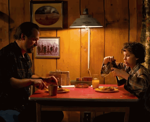 A Man And A Boy Are Sitting At A Table With Plates Of Food GIF