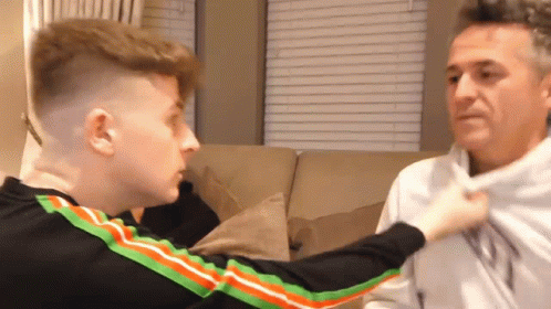 a man and a boy are sitting on a couch and the boy is holding the man 's shirt .