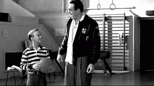 A Man And A Boy Are Standing Next To Each Other In A Gym . The Boy Is Holding A Piece Of Paper . GIF