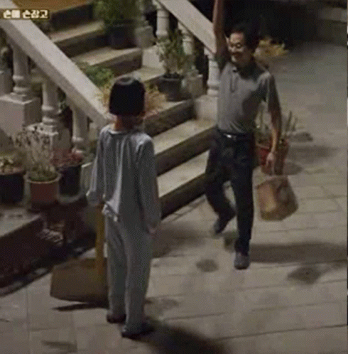 A Man And A Boy Are Standing On A Sidewalk Next To Stairs . GIF