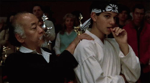 A Man And A Boy In Karate Uniforms Are Standing Next To Each Other In A Crowd GIF