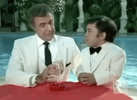 A Man And A Boy In Tuxedos Are Sitting At A Table With A Glass Of Champagne . GIF