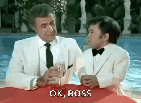 A Man And A Boy In Tuxedos Are Sitting At A Table With A Glass Of Wine And Talking . GIF