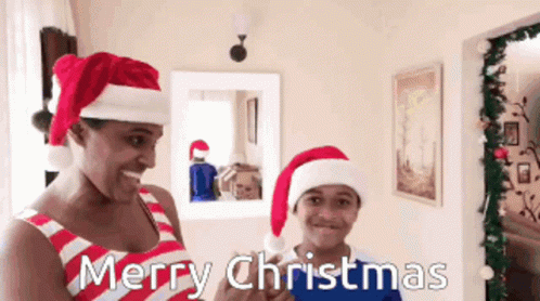 A Man And A Boy Wearing Santa Hats Say Merry Christmas In A Living Room GIF