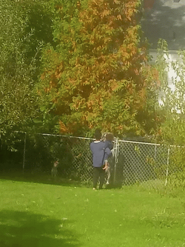 A Man And A Child Are Standing In Front Of A Chain Link Fence In A Park GIF