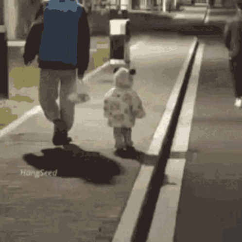 A Man And A Child Are Walking Down A Street . GIF