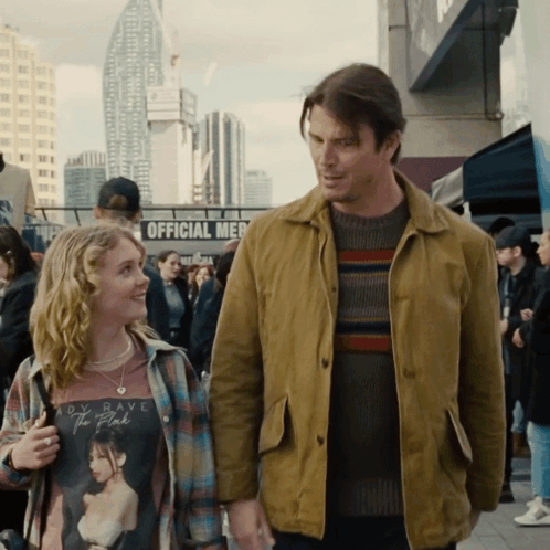 A Man And A Girl Are Standing Next To Each Other In Front Of A Sign That Says Official Merch GIF