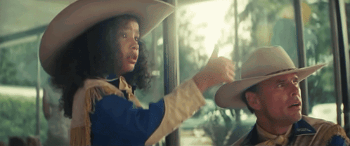A Man And A Girl In Cowboy Hats Are Looking Out A Window GIF