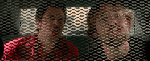 A Man And A Woman Are Behind A Mesh Fence GIF