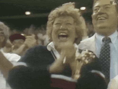 A Man And A Woman Are Clapping In A Crowd With A Mlb Logo In The Corner GIF